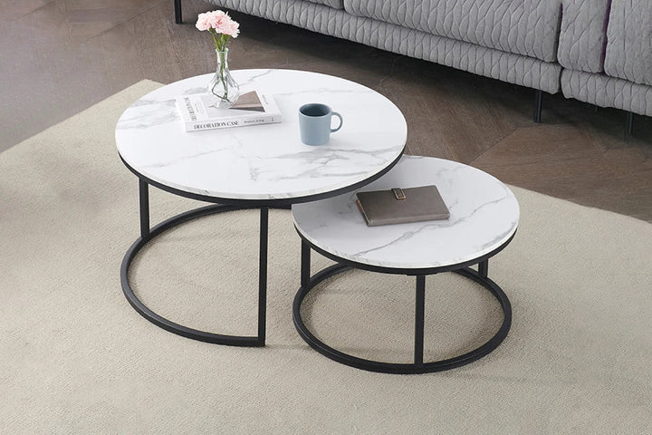 Two nesting coffee tables with a white sintered stone top and black metal base, one larger than the other, placed on a beige carpet.