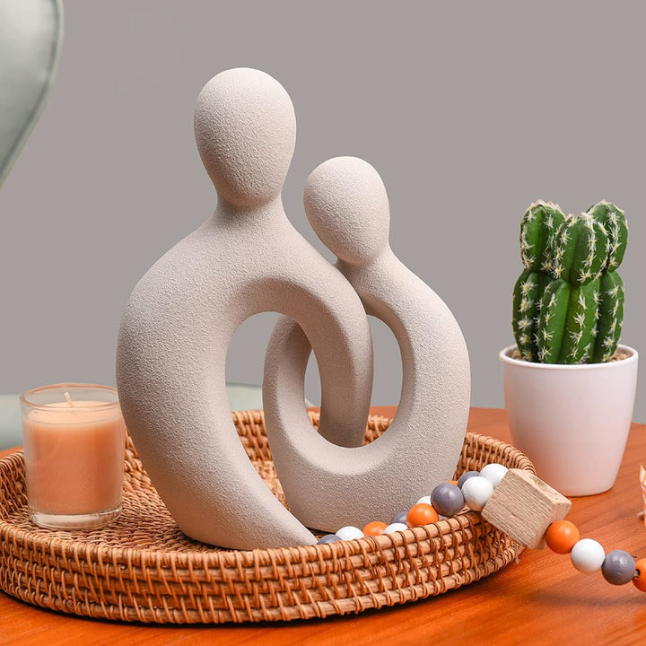 Decorative sculpture of two abstract figures on a tray with a candle and cactus in the background.