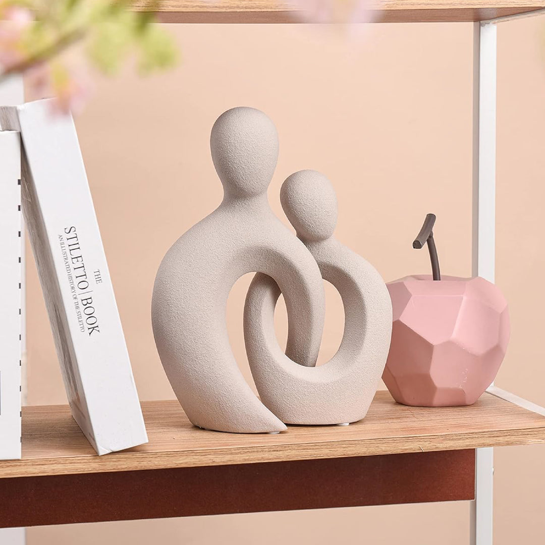 Decorative sculpture of two abstract figures on a shelf with a pink geometric object.