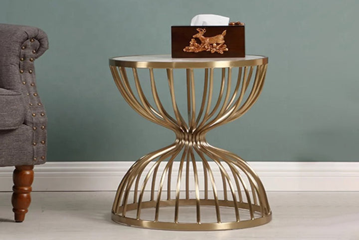 Gold metal side table with a white round top against a gray wall.