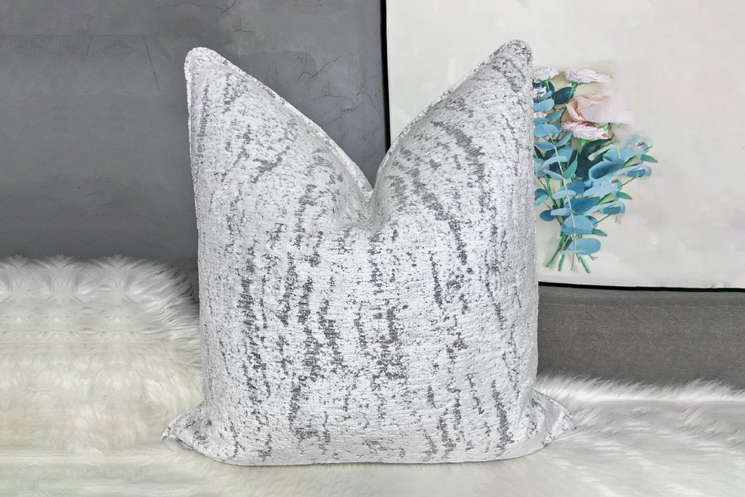 Silver sequin pillow on a textured surface with a blurred background