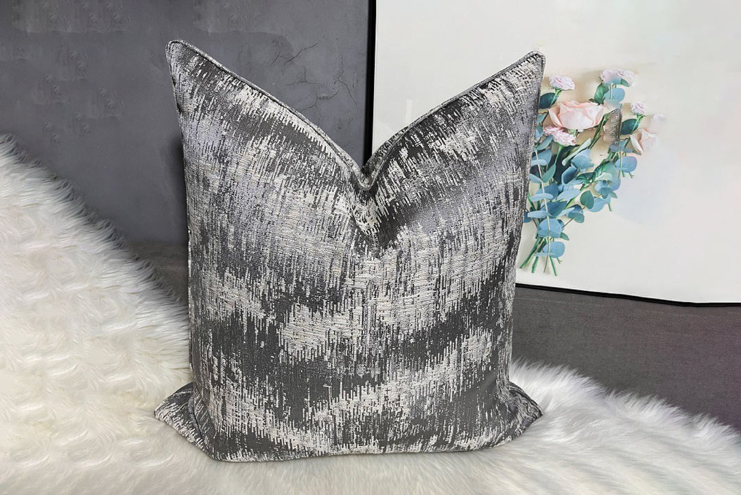 Textured gray pillow on a white surface with a blurred floral painting in the background