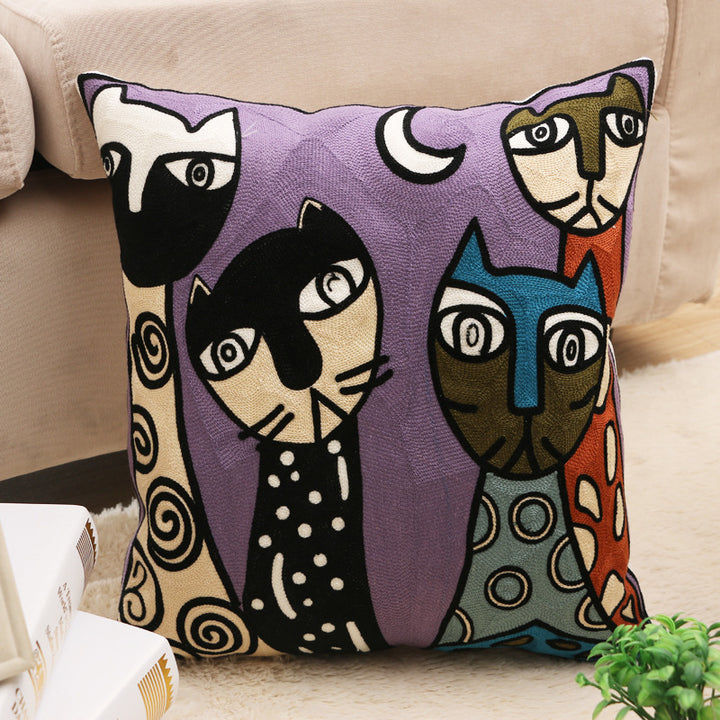 A square-shaped cushion cover featuring a hand-embroidered design with chain stitch, inspired by Picasso's cubism style with various stylized cat faces in multicolor on a purple background.