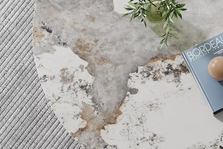 Round marble coffee table with a textured surface, featuring a book and plant.