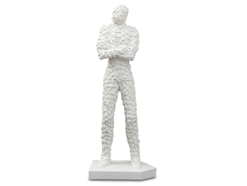 A white sculpture of a standing brick man with crossed arms, made from sandstone, displayed on a white base.