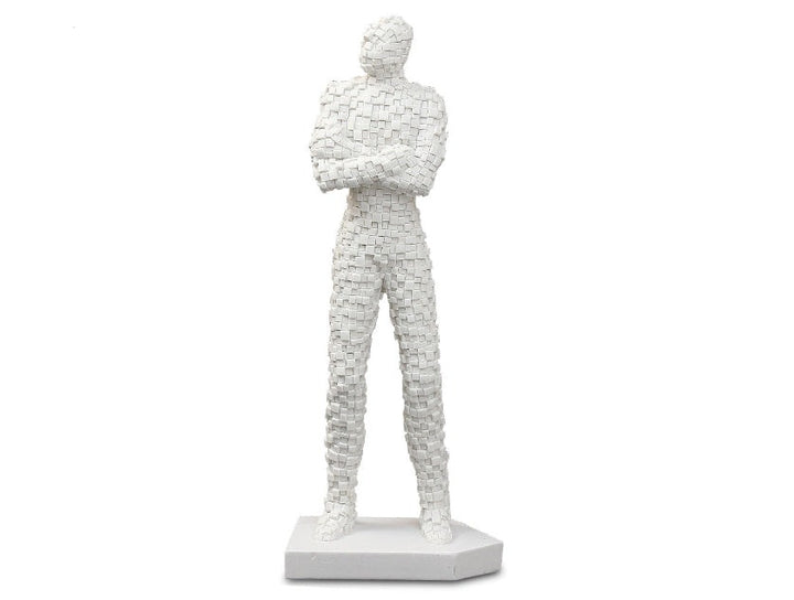 A white sculpture of a standing brick man with crossed arms, made from sandstone, displayed on a white base.
