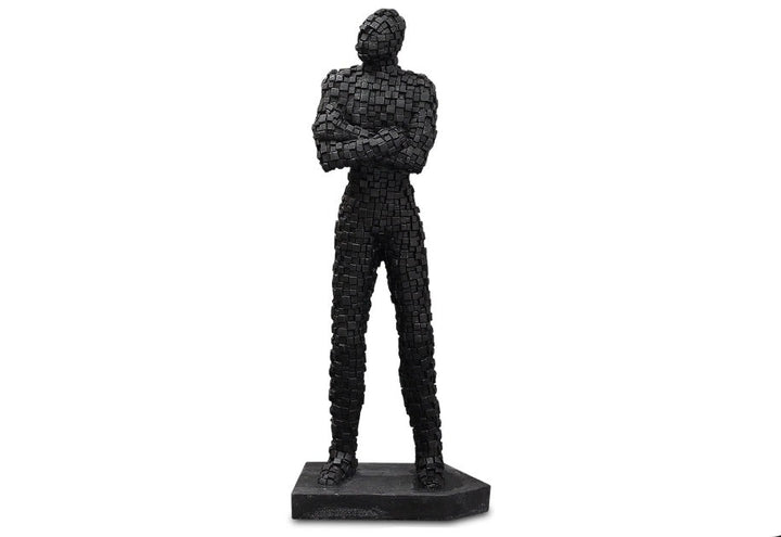 A black brickman figurine standing with arms crossed, made of sandstone with a mosaic texture.