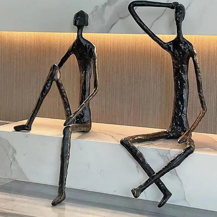 Two abstract sculptures of people on a marble surface with a neutral background