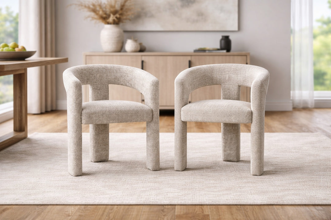 Two beige chairs on a light rug in a room with a wooden sideboard and window.