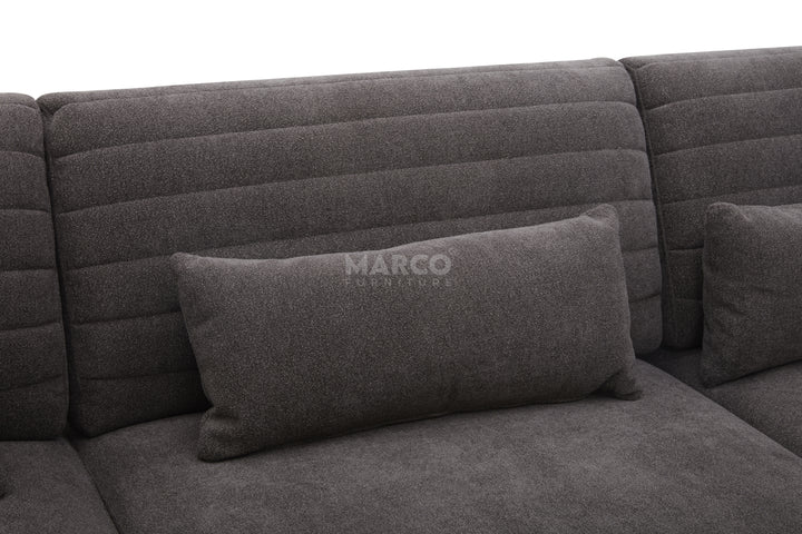 Gray sectional sofa with a pillow featuring the brand 'Marco' on a dark background