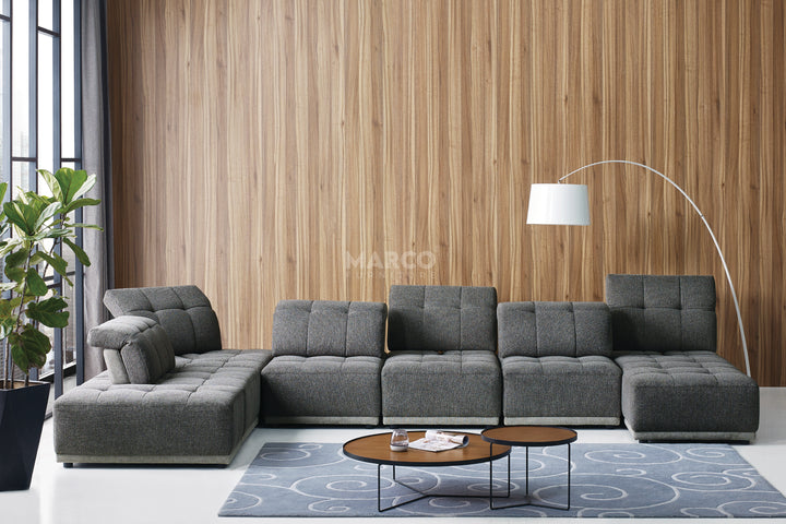 Gray sectional sofa in a living room with a wooden wall and a lamp.