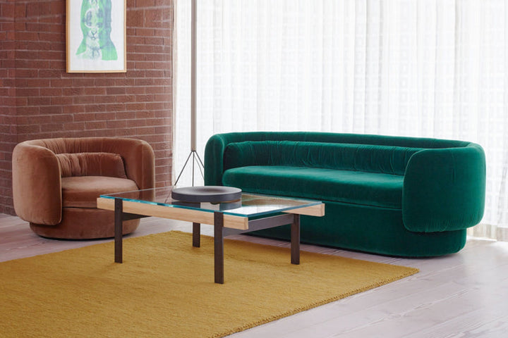 Modern living room with a green sofa, brown armchair, and glass coffee table.